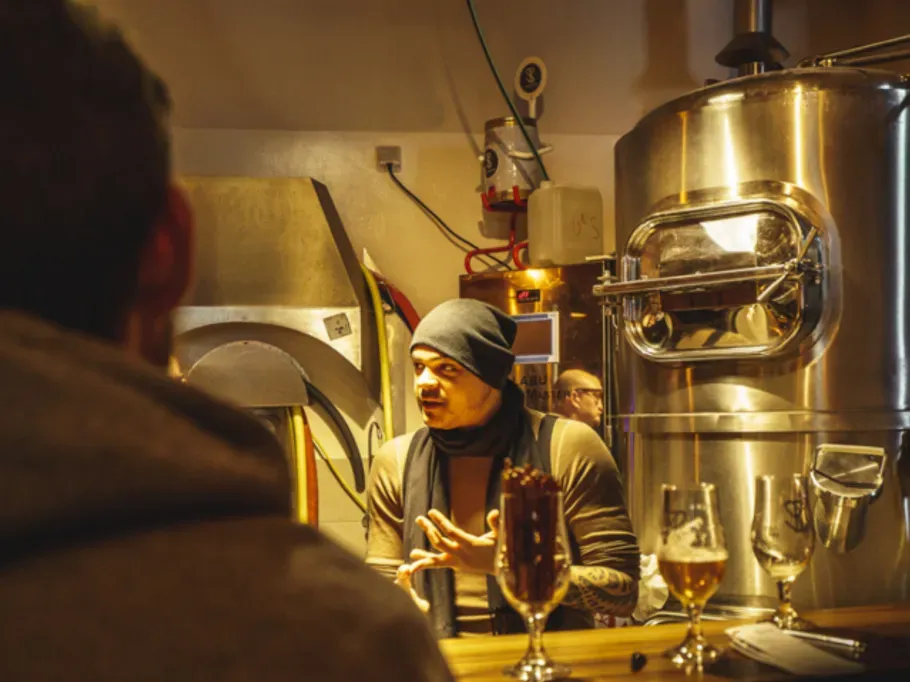 Ein Mann steht vor Bieranlagen und erklärt seiner Gruppe etwas