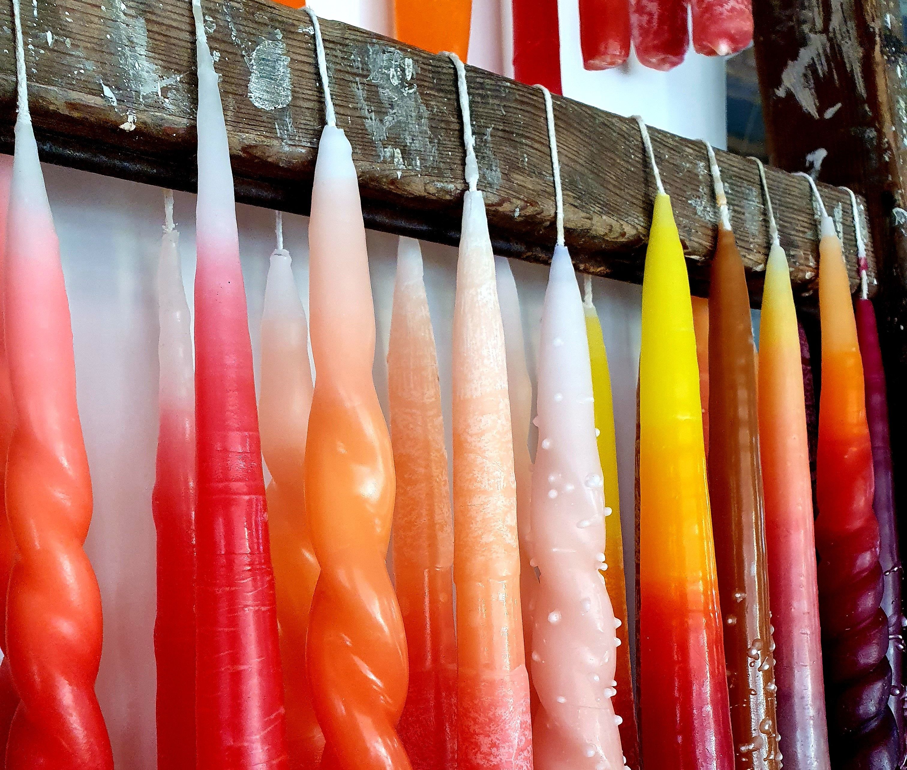 Rote Stabkerzen hängen zum trocknen an einer Leiste