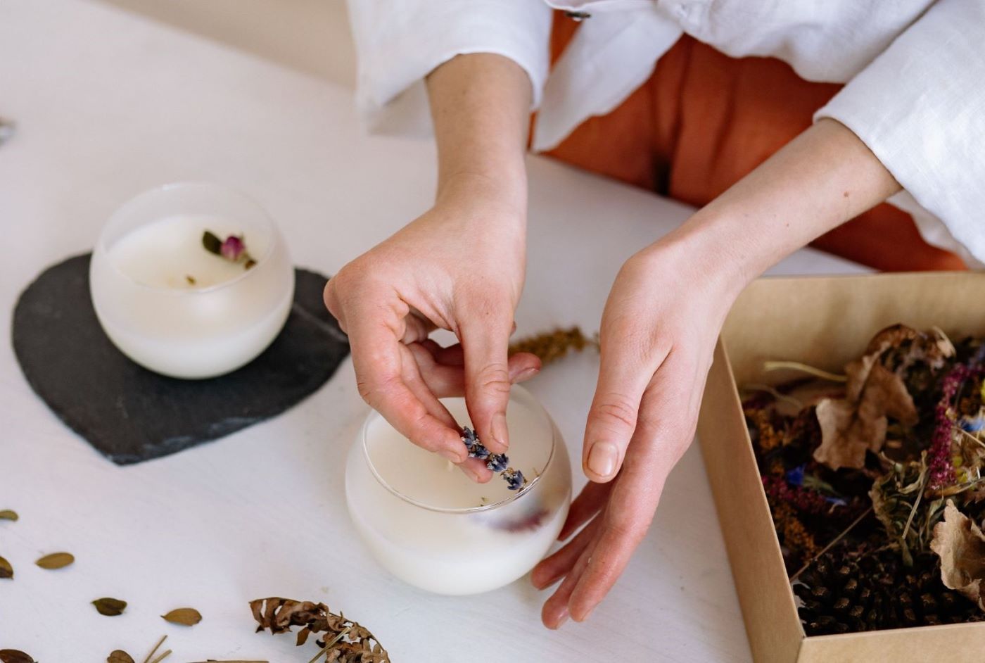 Jemand verziert weiße Kerzen mit Trockenblumen