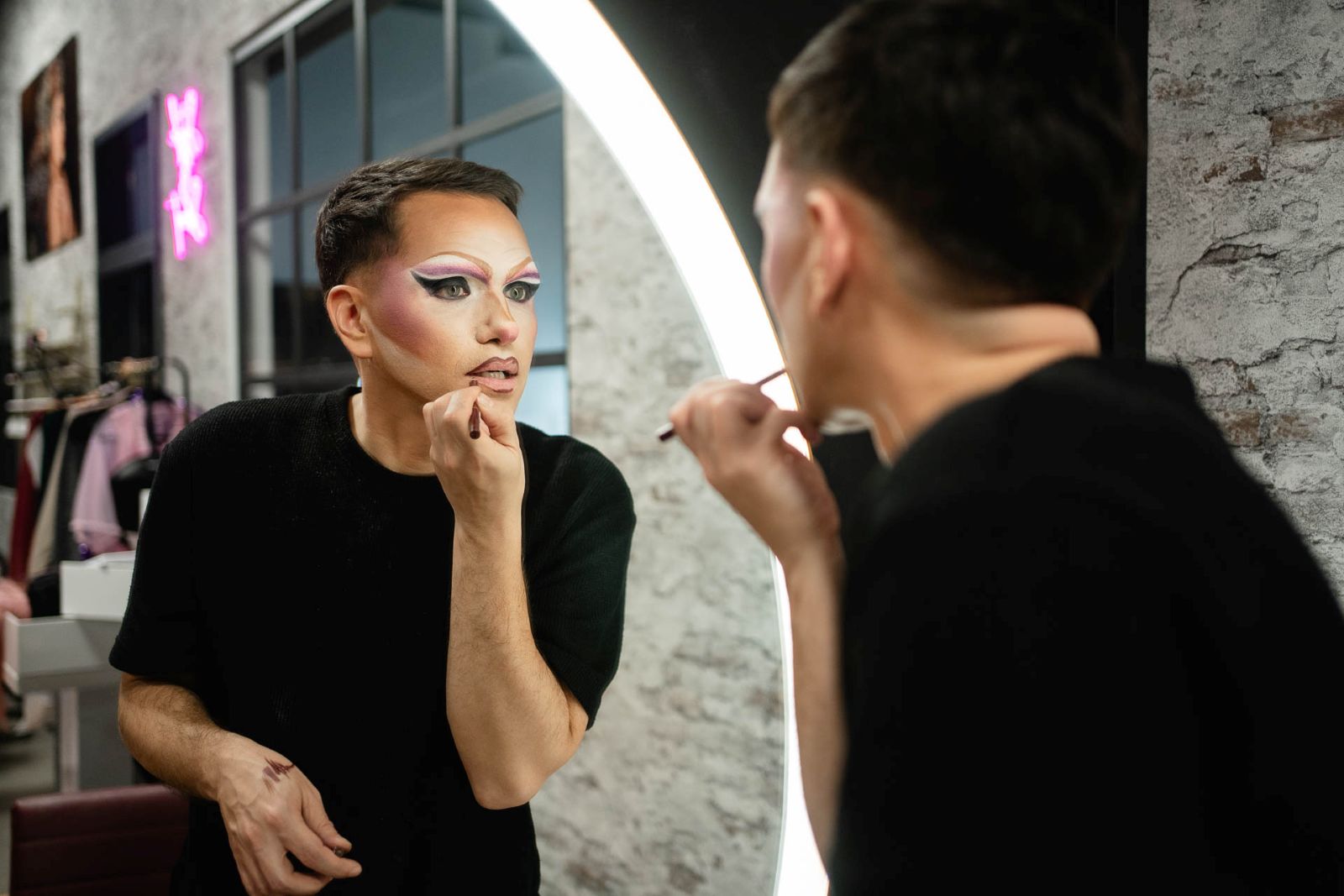 Mann schminkt sich die Lippen vor einem Spiegel.