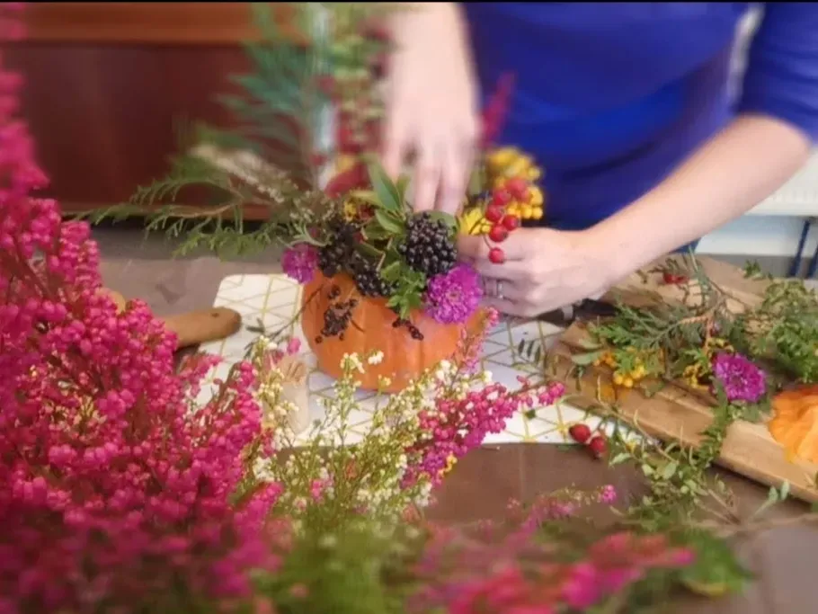 Eine Person steckt Blumen in einen Kürbis.