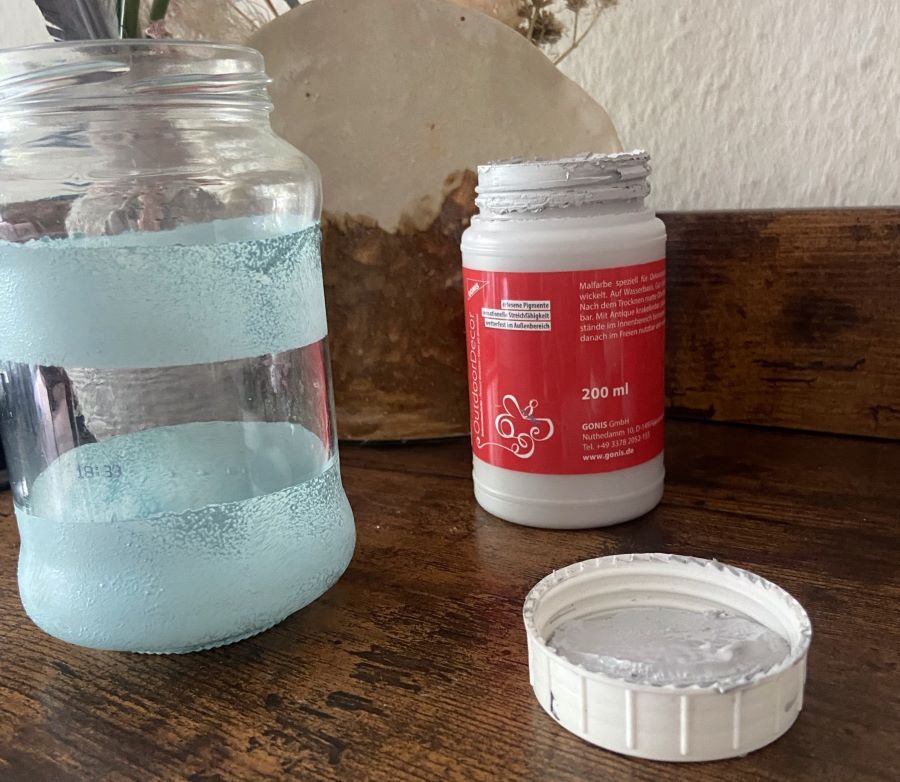 Ein Glas mit blauen Streifen und ein Tiegel mit Farbe