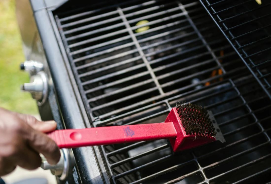 Eine Person macht einen Gasgrill mit einer Bürste sauber.