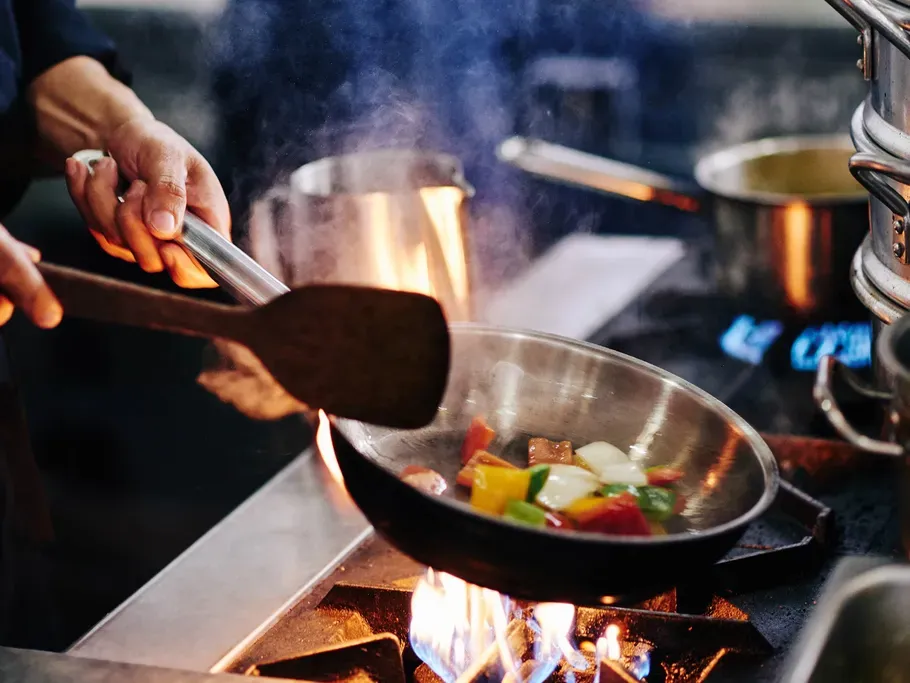 Jemand bereitet Gemüse über der Gasherdflamme zu