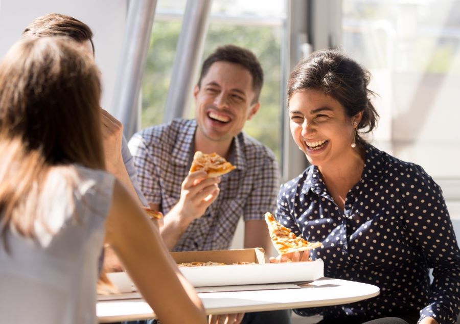 Vier Personen an einem Tisch lachen und essen Pizza
