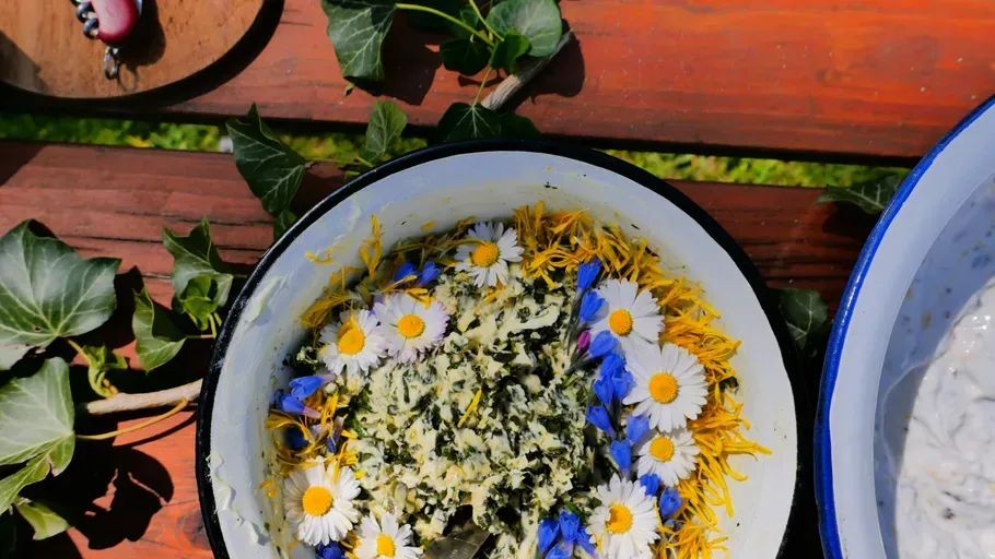 Schale mit frischen Kräutern und Blumen steht auf einer Holzbank