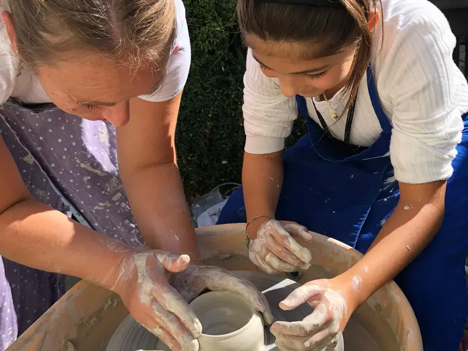 Eine Mutter töpfert mit ihrem Kind an der Drehscheibe. 